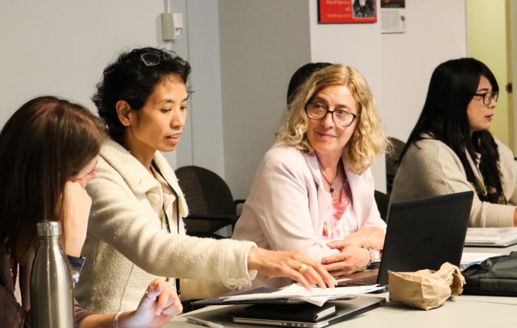 Students seated next to one another at a table speaking