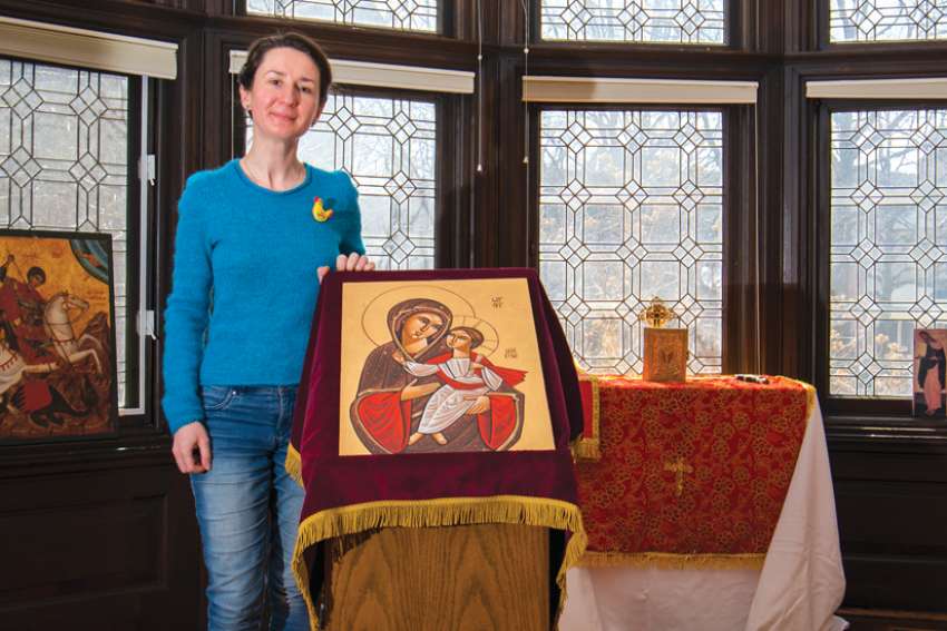 A woman stands indoors next to an icon in front of an altar and a set of bay windows